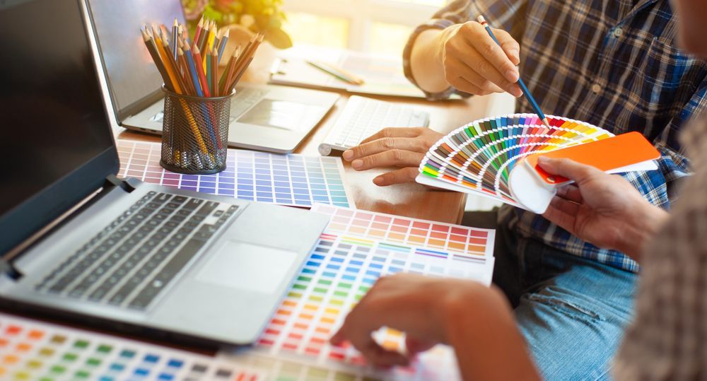 A couple of people are sitting at a table with a laptop and a palette of colors.