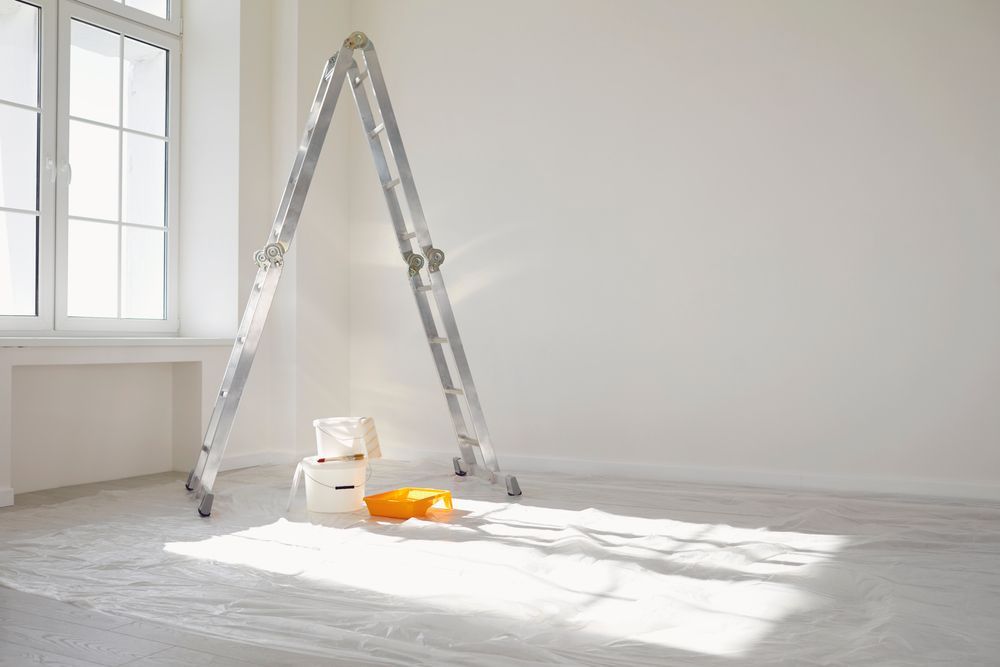 An empty room with a ladder and paint buckets on the floor.