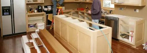 A man is working on a kitchen with wooden cabinets.