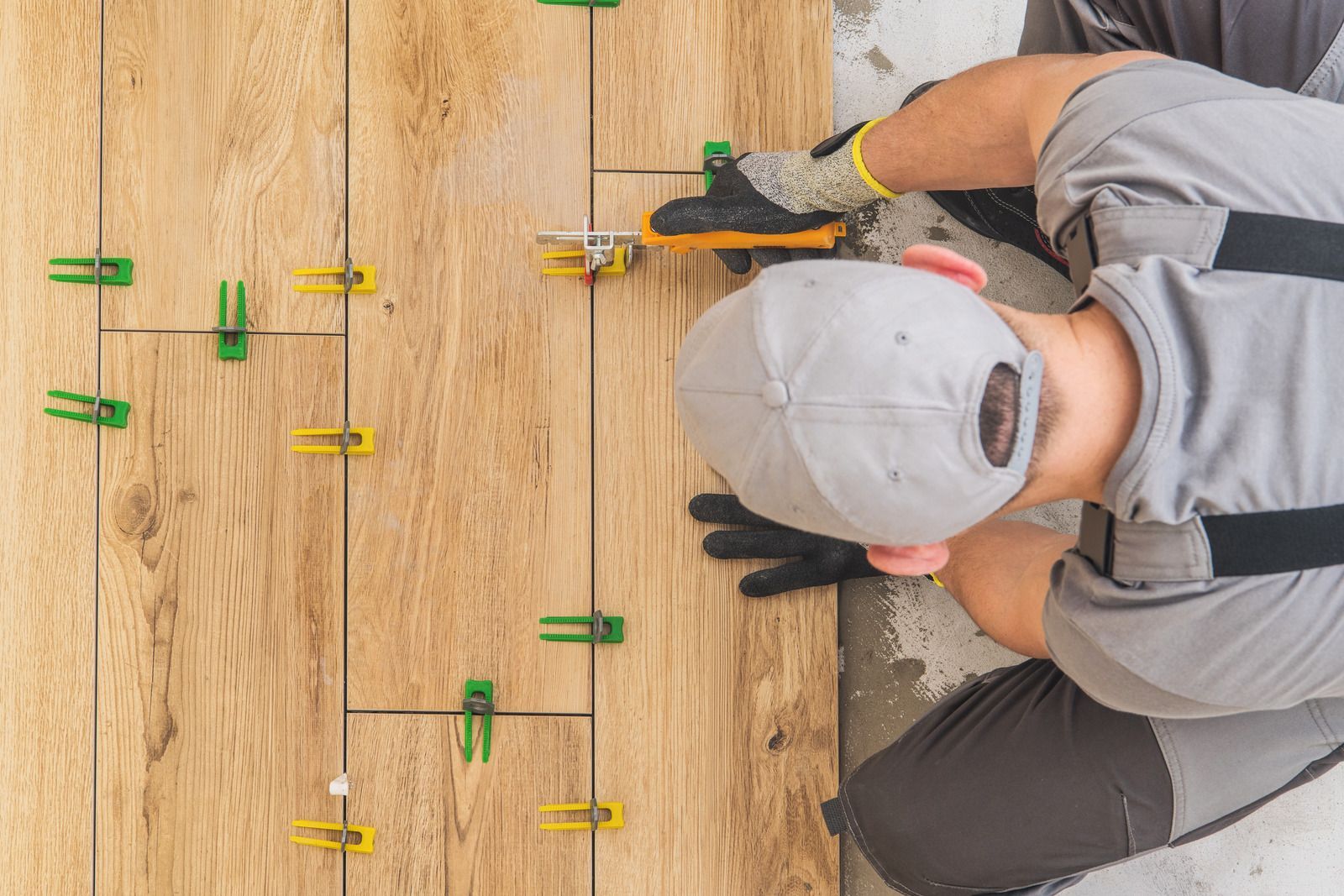 A man is laying tiles on a wooden floor.