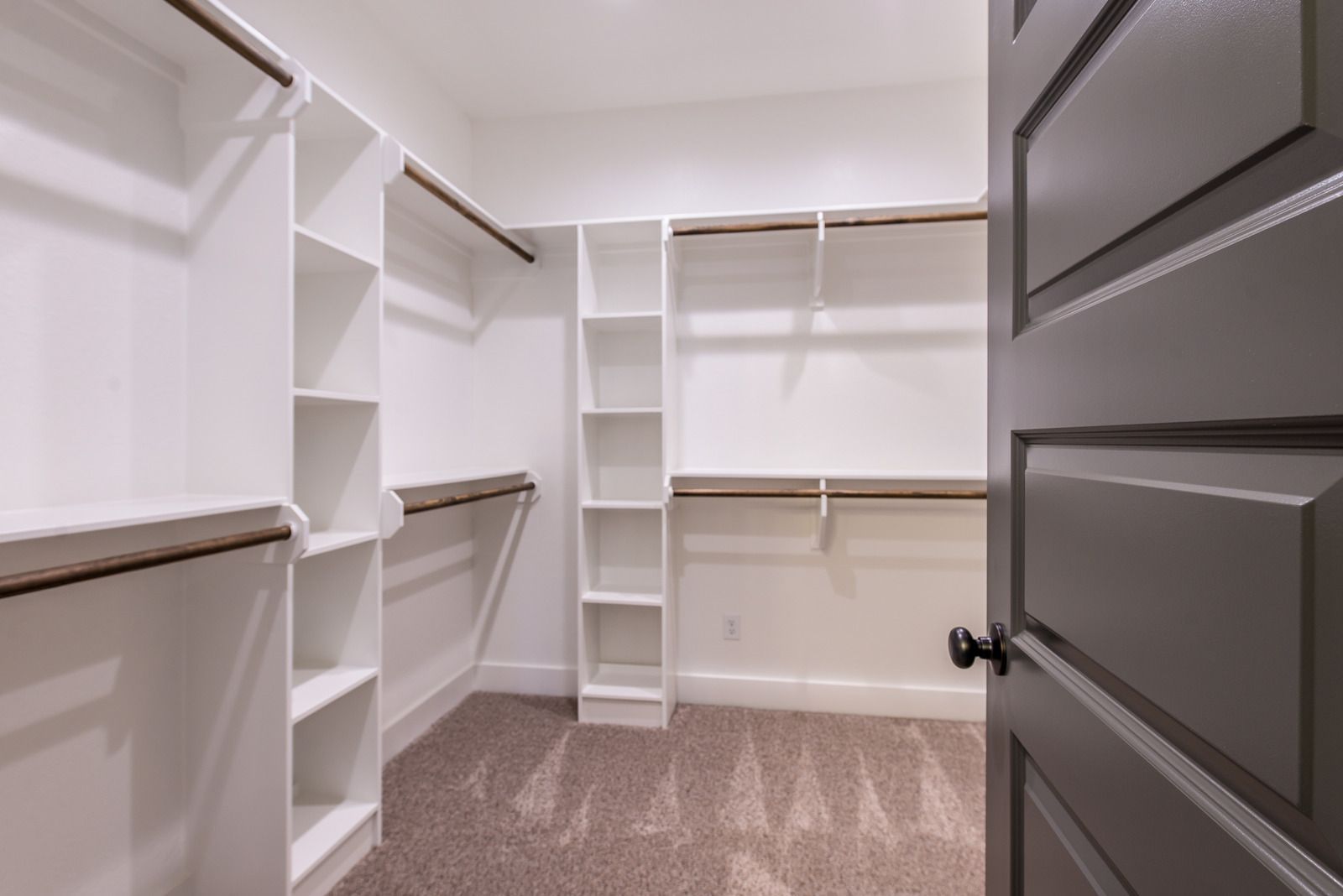 A walk in closet with a gray door and white shelves.