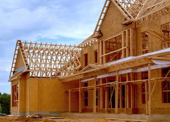 A large wooden house is being built with a blue sky in the background.