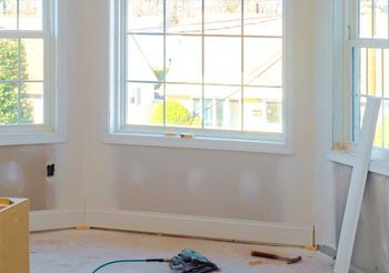 An empty room with two windows and a hammer on the floor.