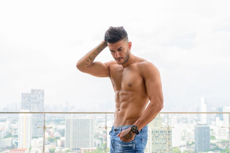 A shirtless man is standing on a balcony overlooking a city.