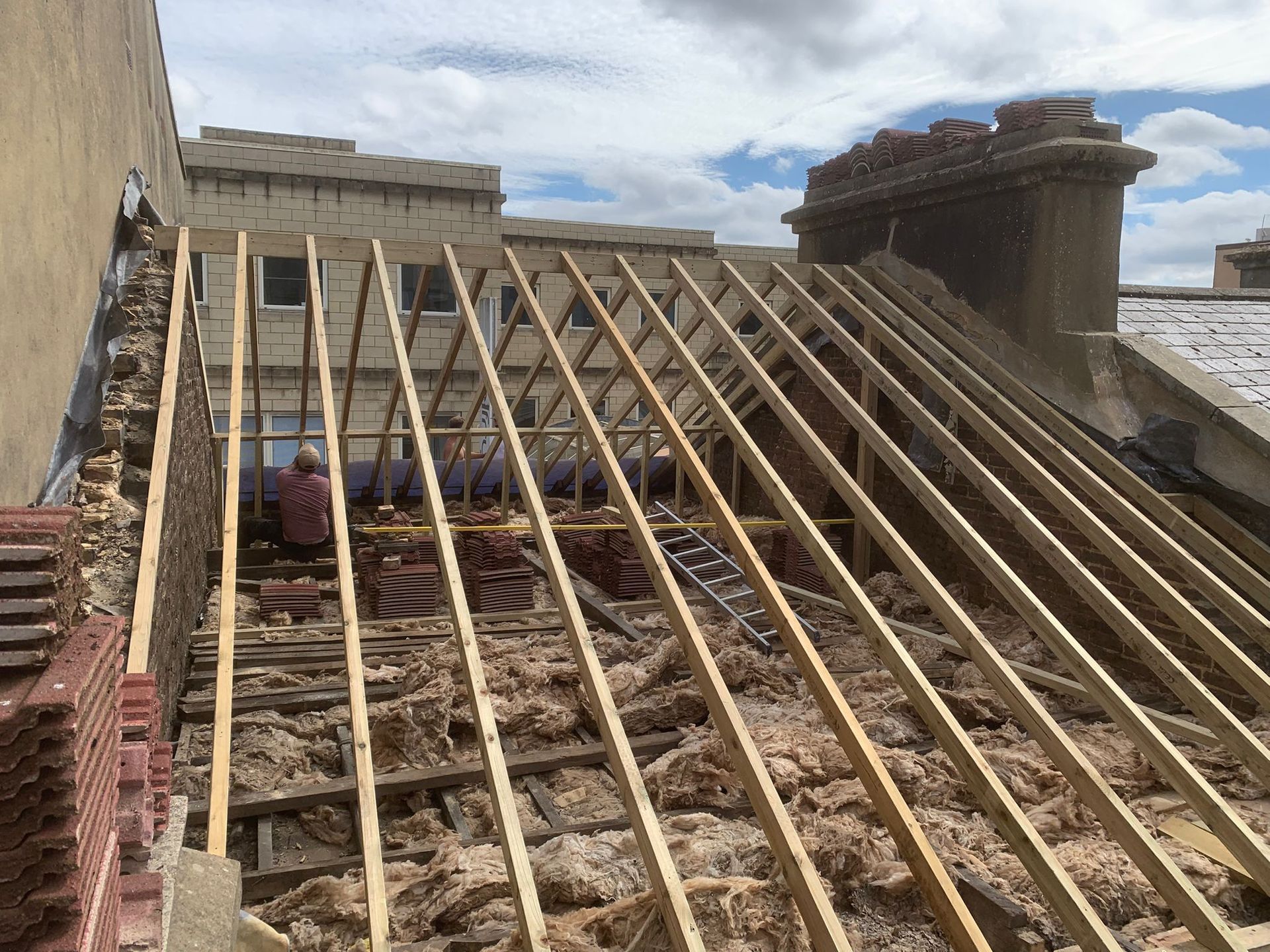 Construction worker, in orange vest and blue helmet, hammering on a rooftop.