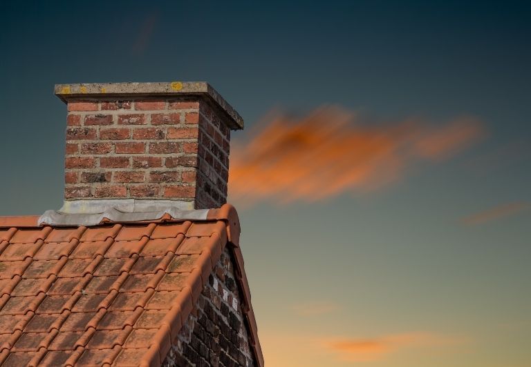 Chimney on a red tiled roof being repaired, covered by a tarp, with scaffolding.
