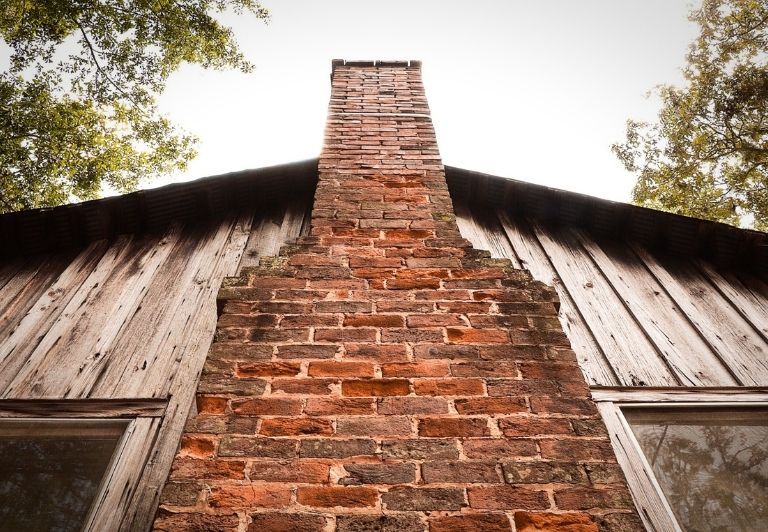 Brick chimney ruin in a forest setting; weathered, with foliage growing on it.