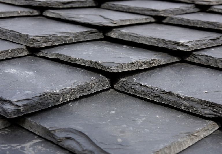 Gray slate roof with damaged flashing, brick wall and skylight.