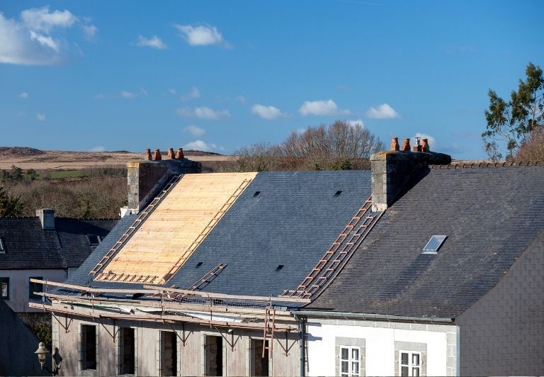 Construction site: partially built house with workers on roof and scaffolding, green field in background.