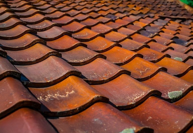Person in gloves repairing a brown tile roof with pliers.