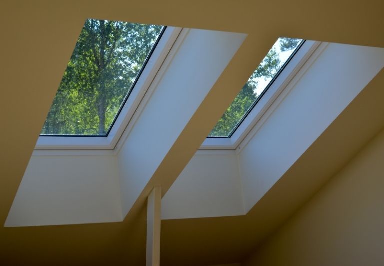 Roofer in safety vest installing roof tiles near skylight on a partially completed roof.