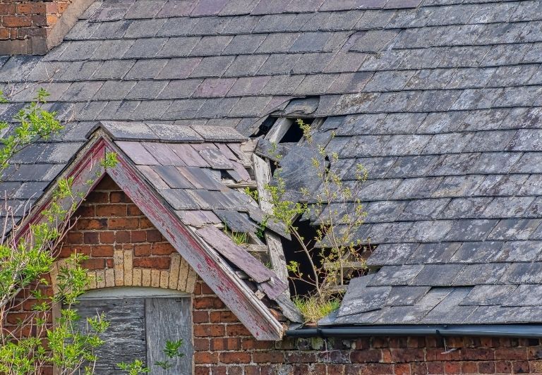 Person using a caulk gun to seal the gap between a window frame and red roof tiles, wearing gloves.
