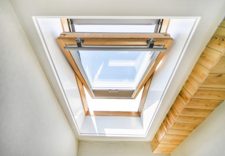 Two skylight windows with wooden frames angled in a white room, blue sky visible.