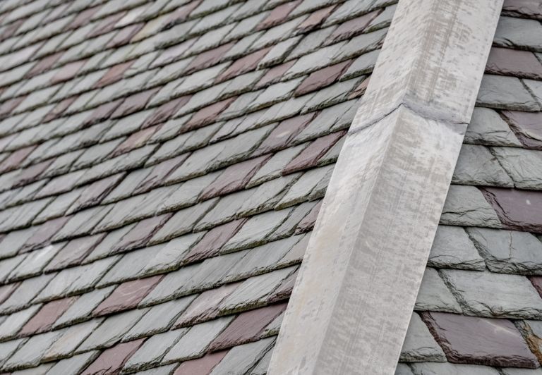 Close-up of a slate roof with jagged edges against a partly cloudy blue sky.
