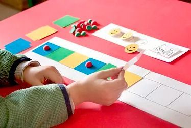 Niño organizando fichas de colores y fichas en una tira de papel en una mesa roja.