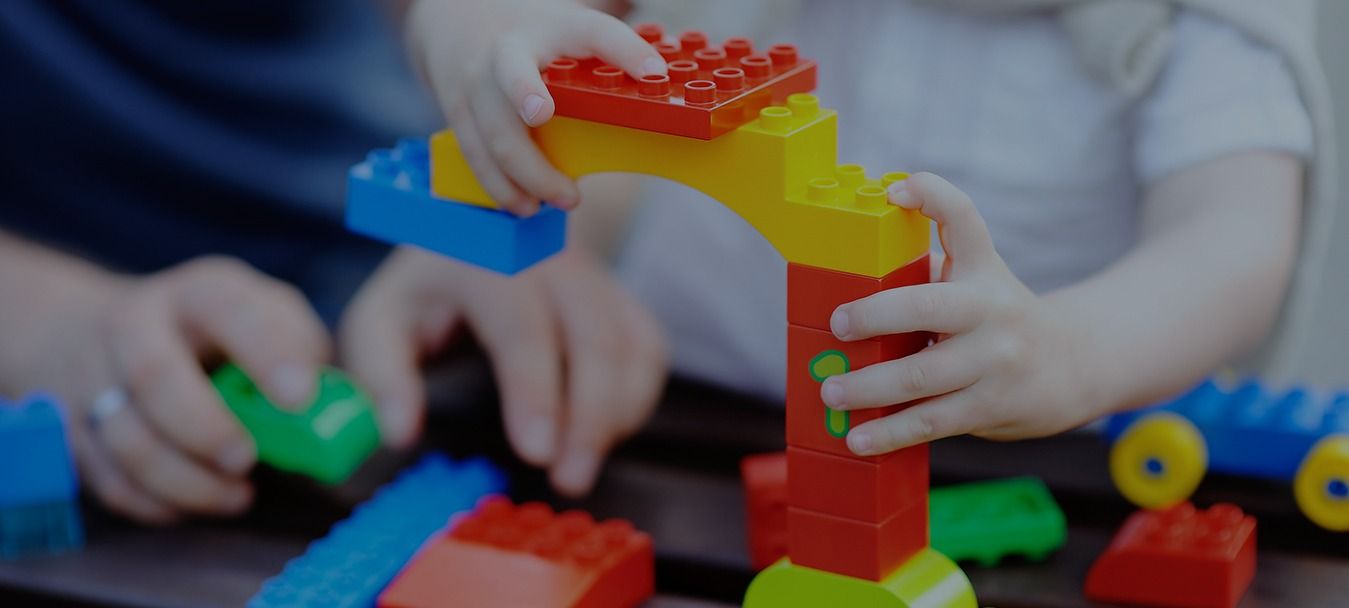 Manos de un niño y un adulto jugando con bloques de construcción de colores.