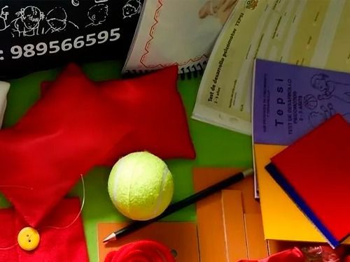 Objetos rojos, pelota de tenis, lápiz, papeles sobre una superficie verde.