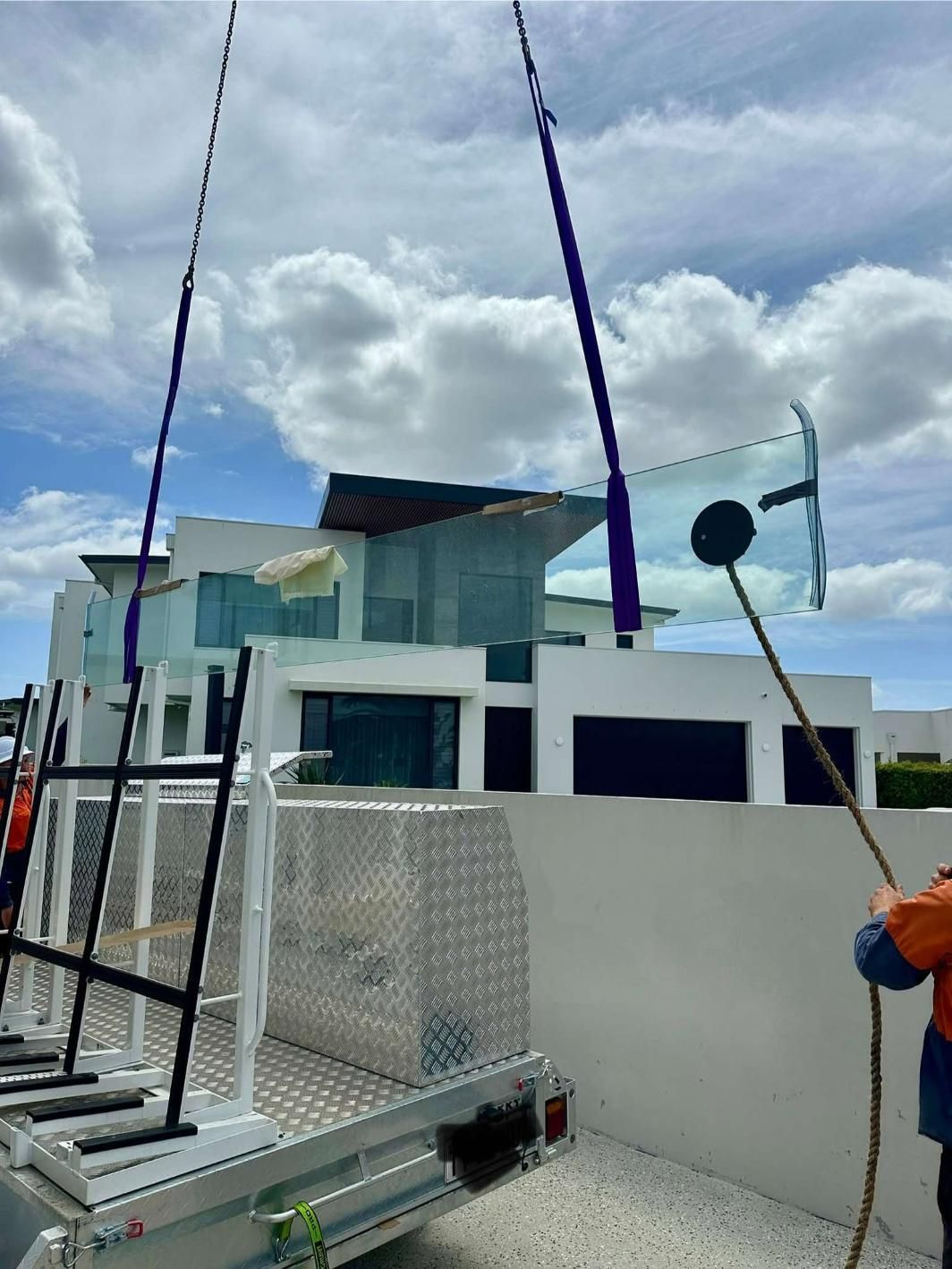 A Man Is Lifting A Glass Railing On A Trailer In Front Of A House — Glass Pool Windows Australia In Tweed Heads, NSW