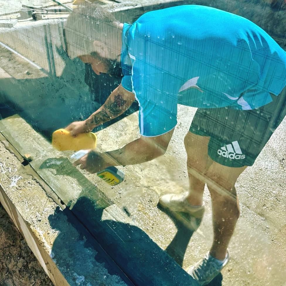 A Man Wearing Adidas Shorts Is Cleaning A Window With A Sponge — Glass Pool Windows Australia In Sunshine Coast, QLD