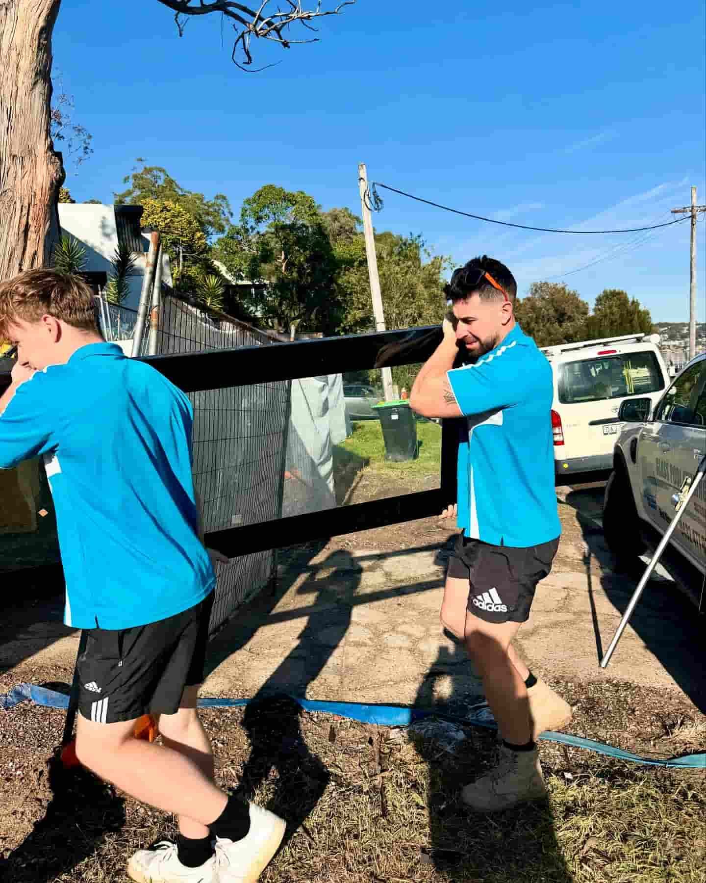 Two People in Blue Shirts Carrying a Large Glass Panel — Glass Pool Windows Australia In Manly, NSW