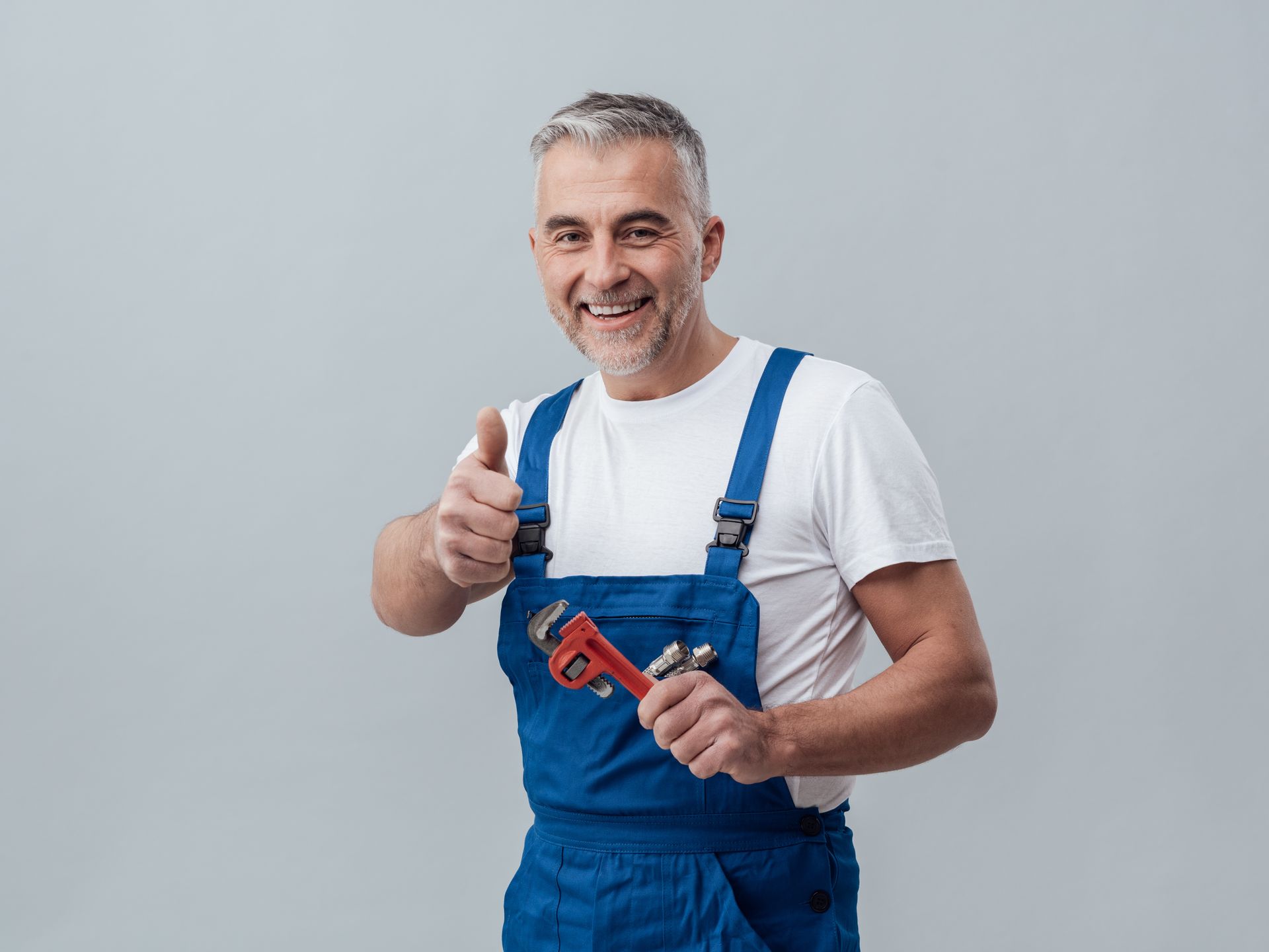 Plumber in blue overalls holding a wrench and giving a thumbs-up gesture.