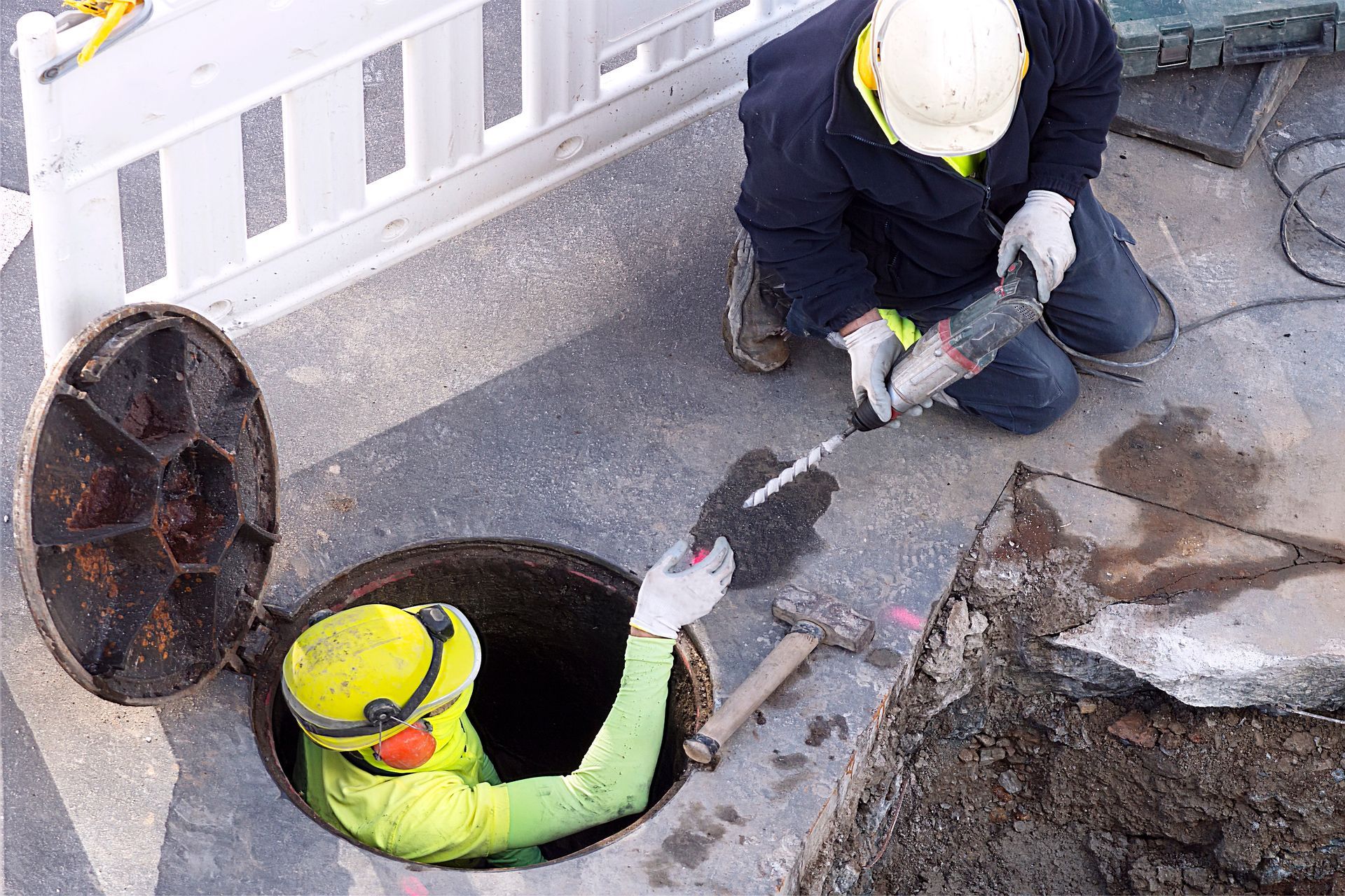 Drain cleaning company workers repairing a sewer manhole and clearing an underground drainage.