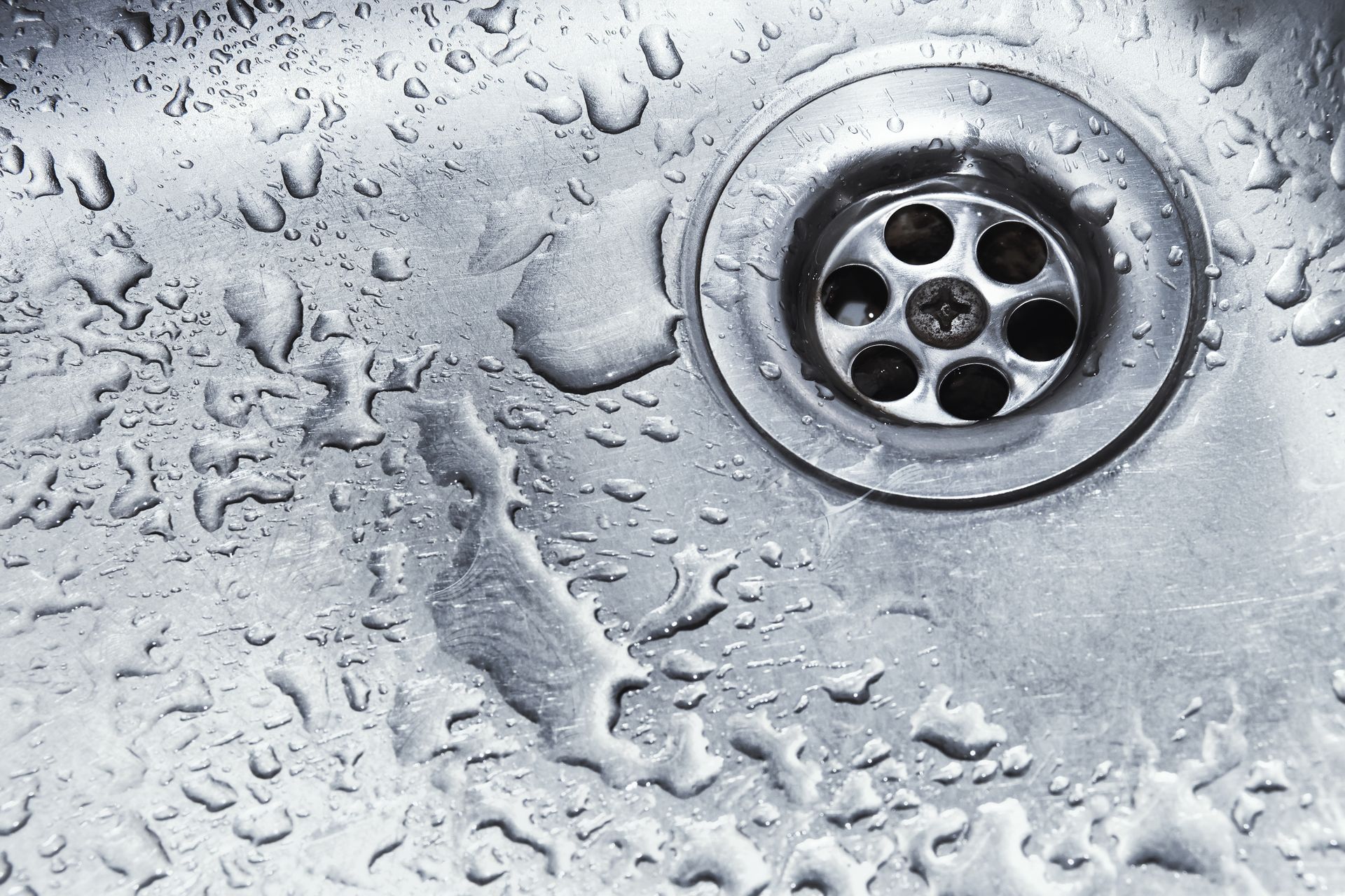 Close-up of water droplets on a metal sink surface near the drain.