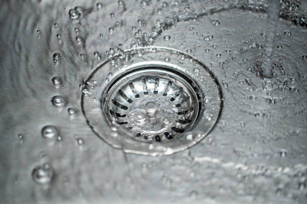 Close-up of water flowing into a stainless steel sink drain.