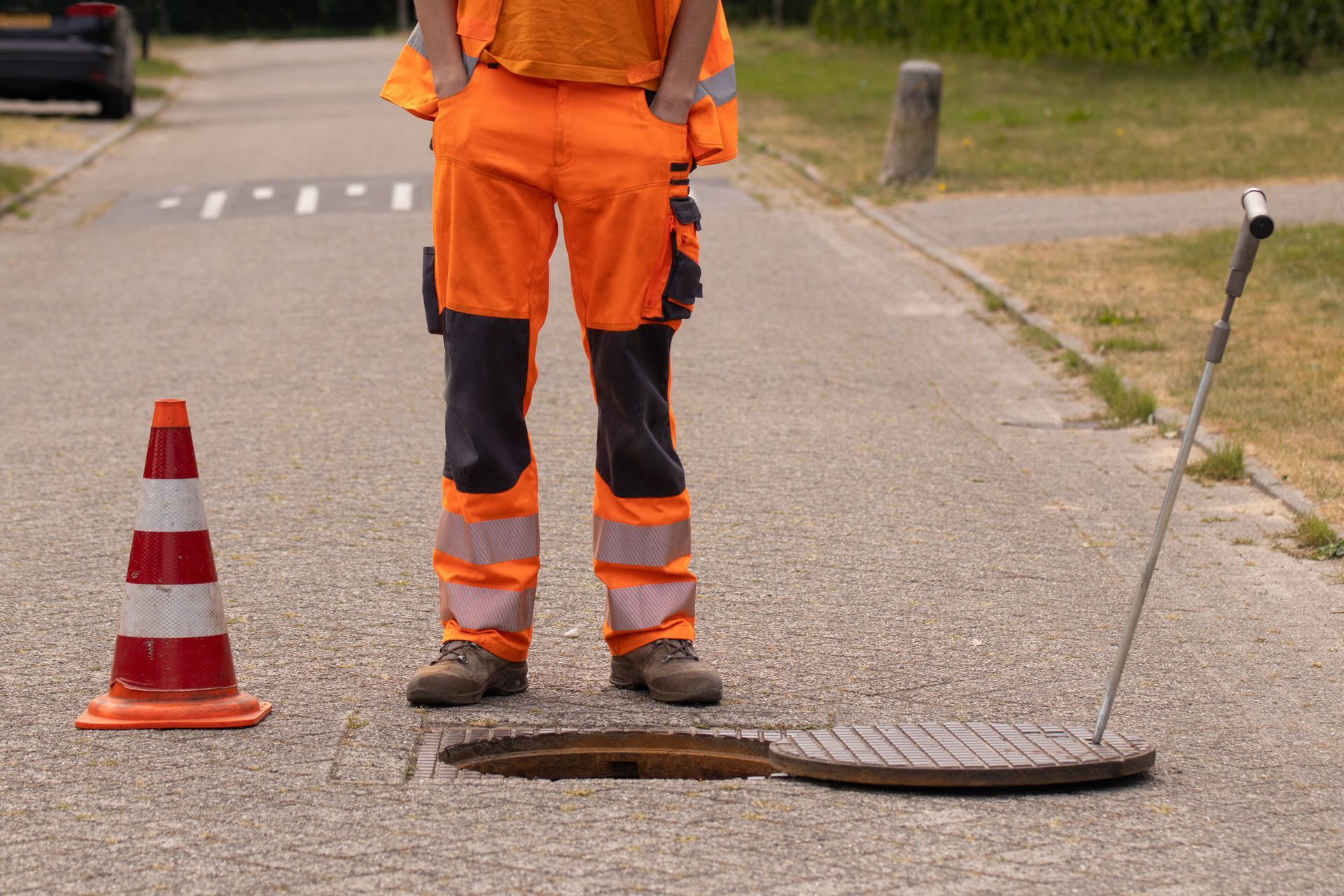 A sewer inspector stands in front of a sewer manhole in the middle of the street.