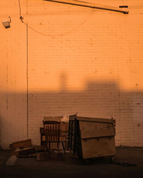 Dilapidated shelter made of cardboard and wood against a brick wall, illuminated by warm light.