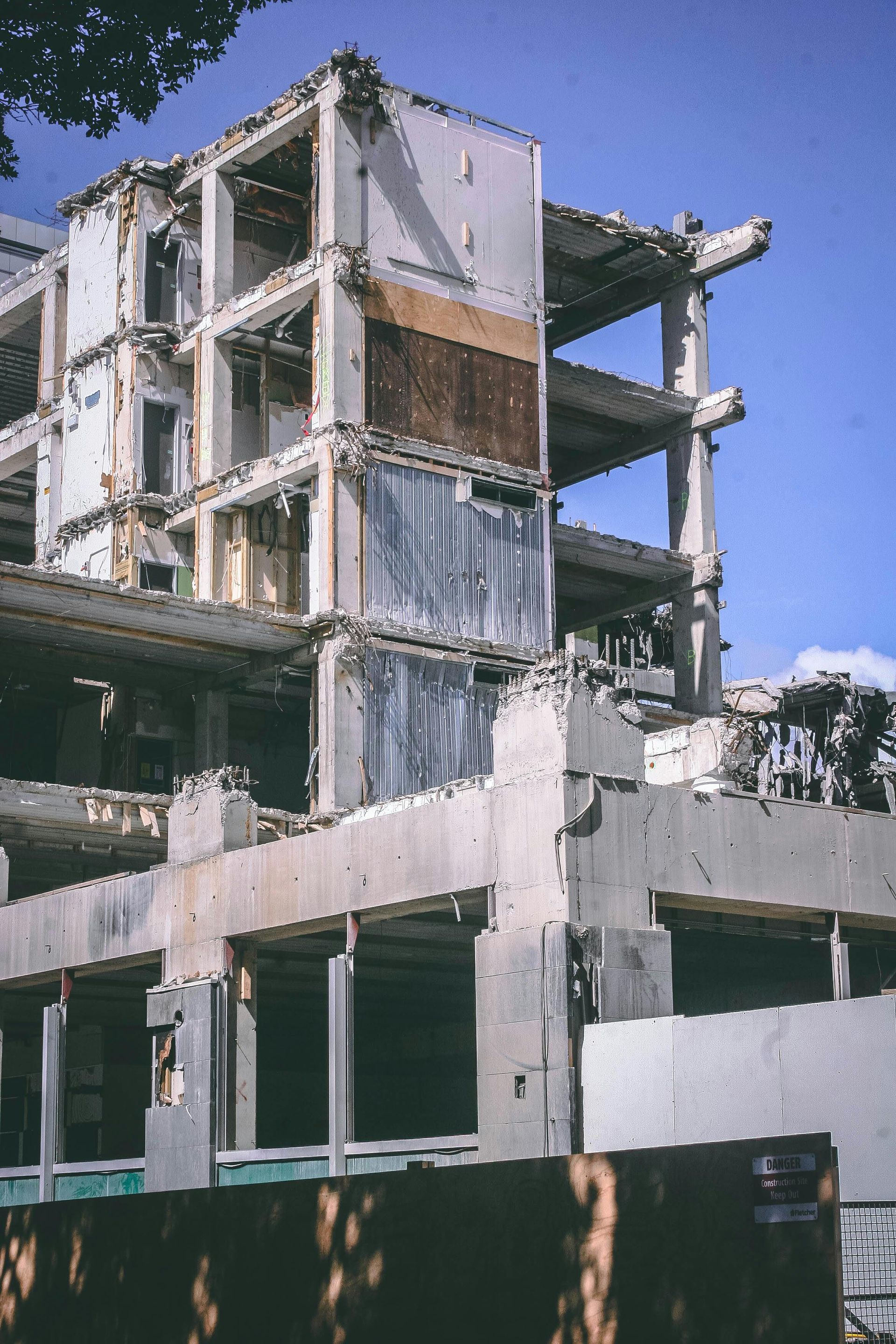 Demolished concrete building with exposed floors and fragmented walls, against a blue sky.