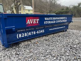 Blue dumpster with AVET Waste Management logo; phone number visible (828) 678-6345, in gravel parking lot.
