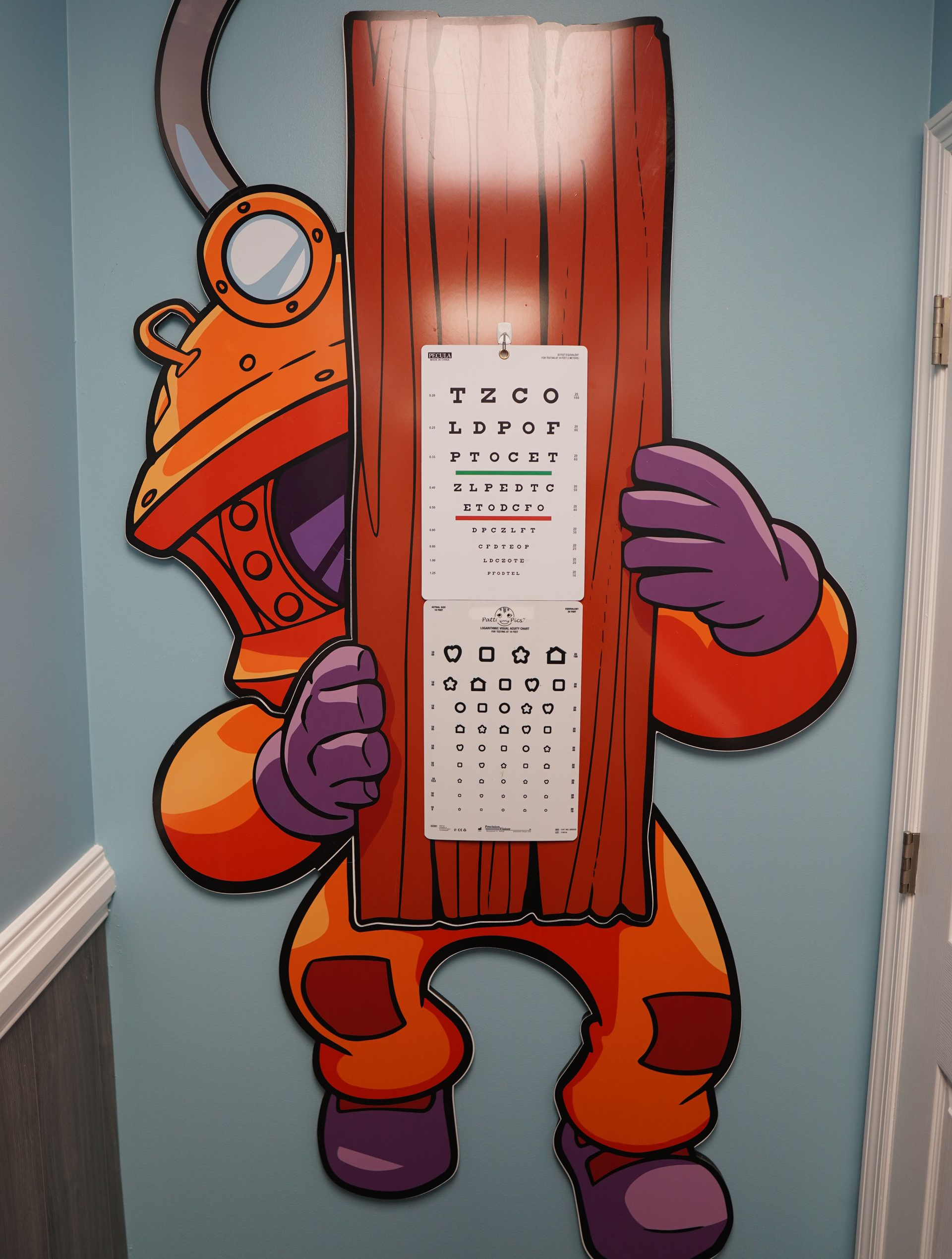 An orange cartoon deep-sea diver holding a wooden board with two eye charts mounted on it against a blue wall.
