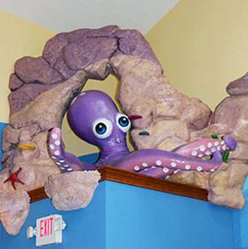 A purple octopus is sitting on a rock next to an exit sign.