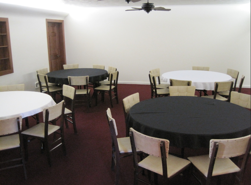 A room with round tables covered in black and white tablecloths, surrounded by chairs.