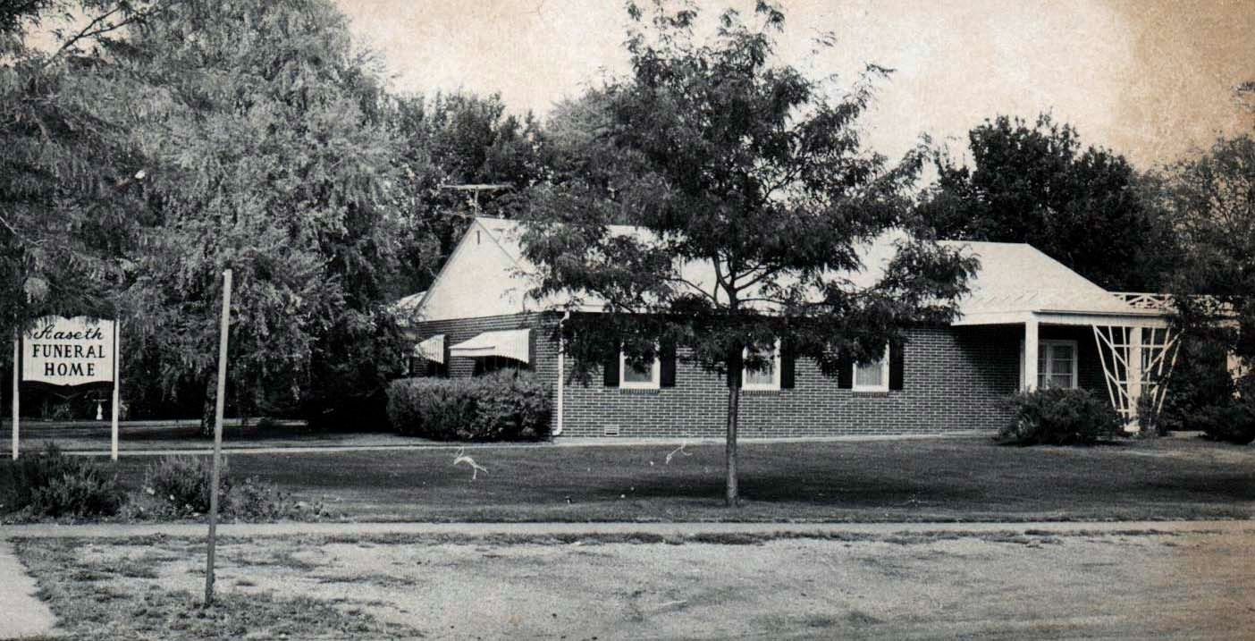 Black and white photo of a small brick building with a sign that reads