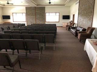 Rows of chairs face a room with windows, a table, and seating.