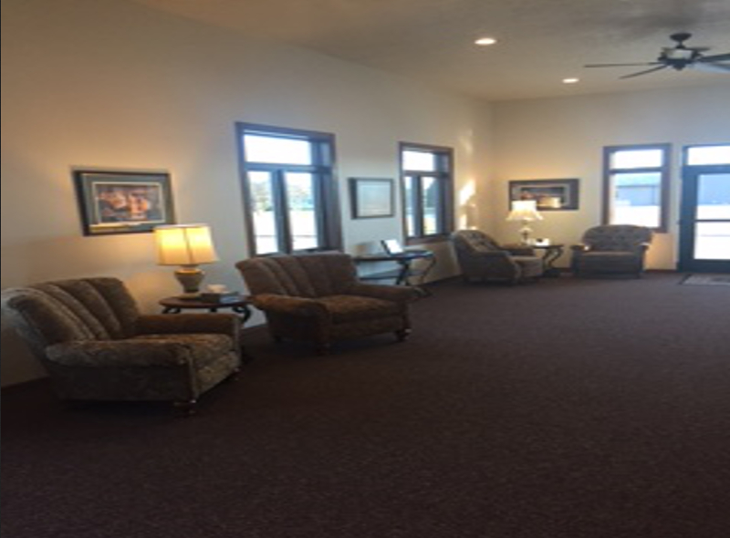 Interior waiting area with armchairs, windows, lamps, and dark carpet.