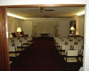 Interior of a funeral home chapel with chairs, a casket area, and lighting.