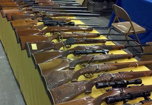 Rifles displayed on a table at an event, with wooden stocks and scopes.