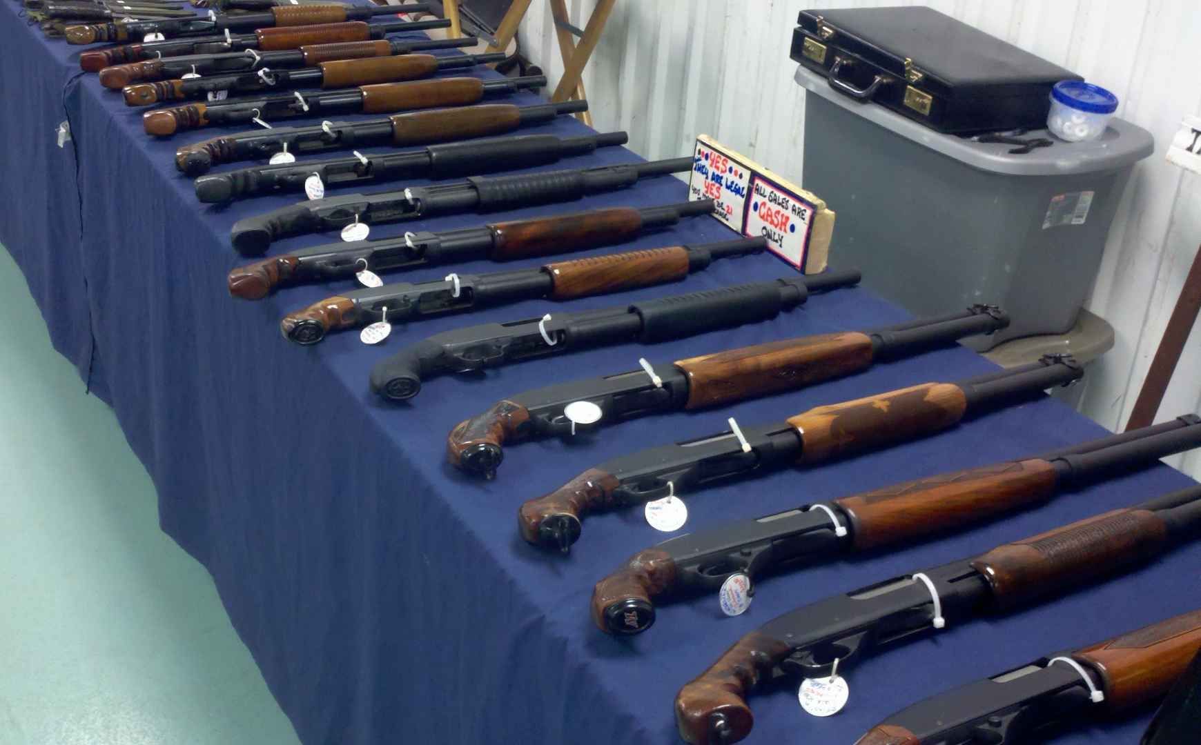 Shotguns displayed on a blue-covered table at what appears to be a gun show.