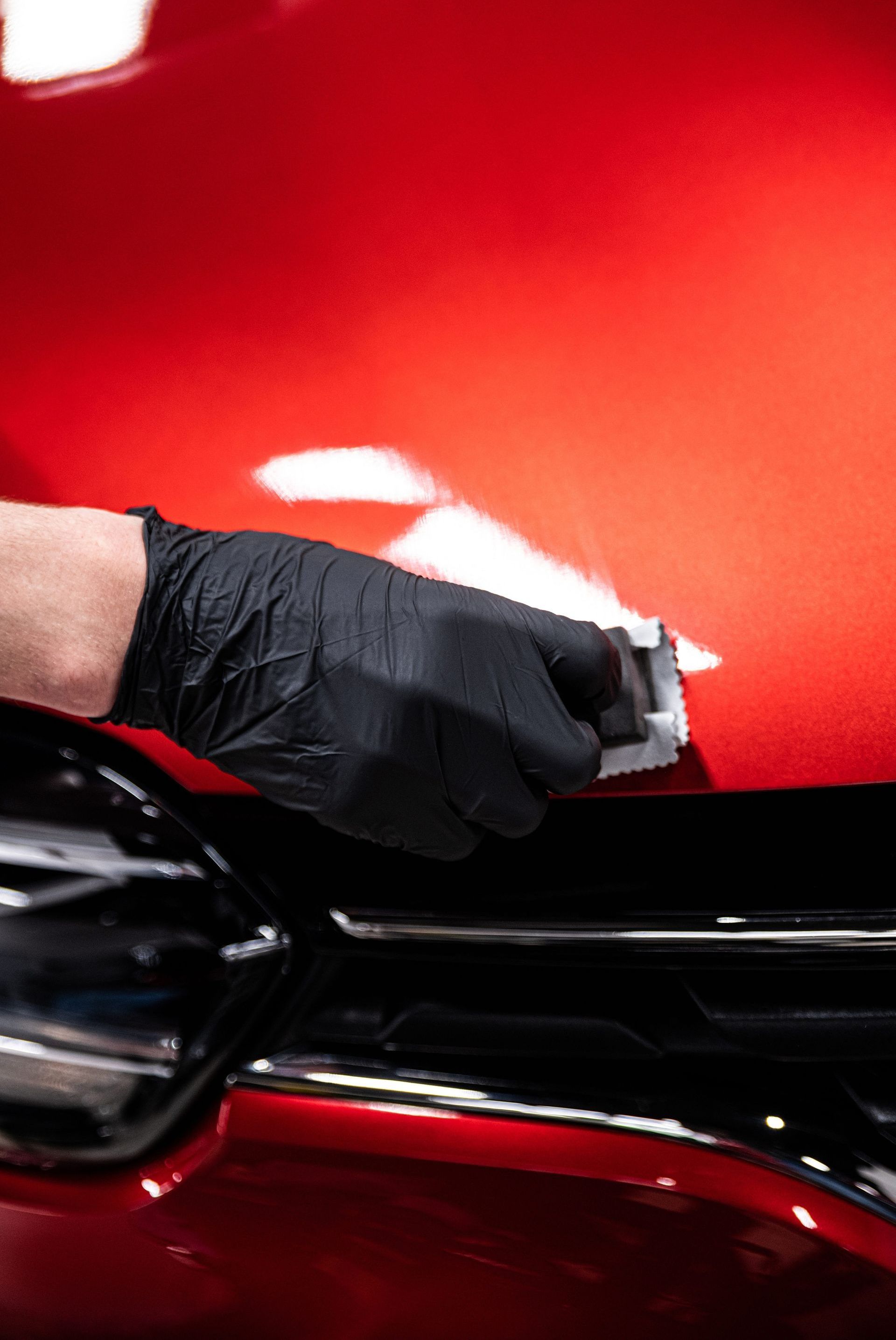 A gloved hand applying a ceramic coating to a red car's shiny surface.