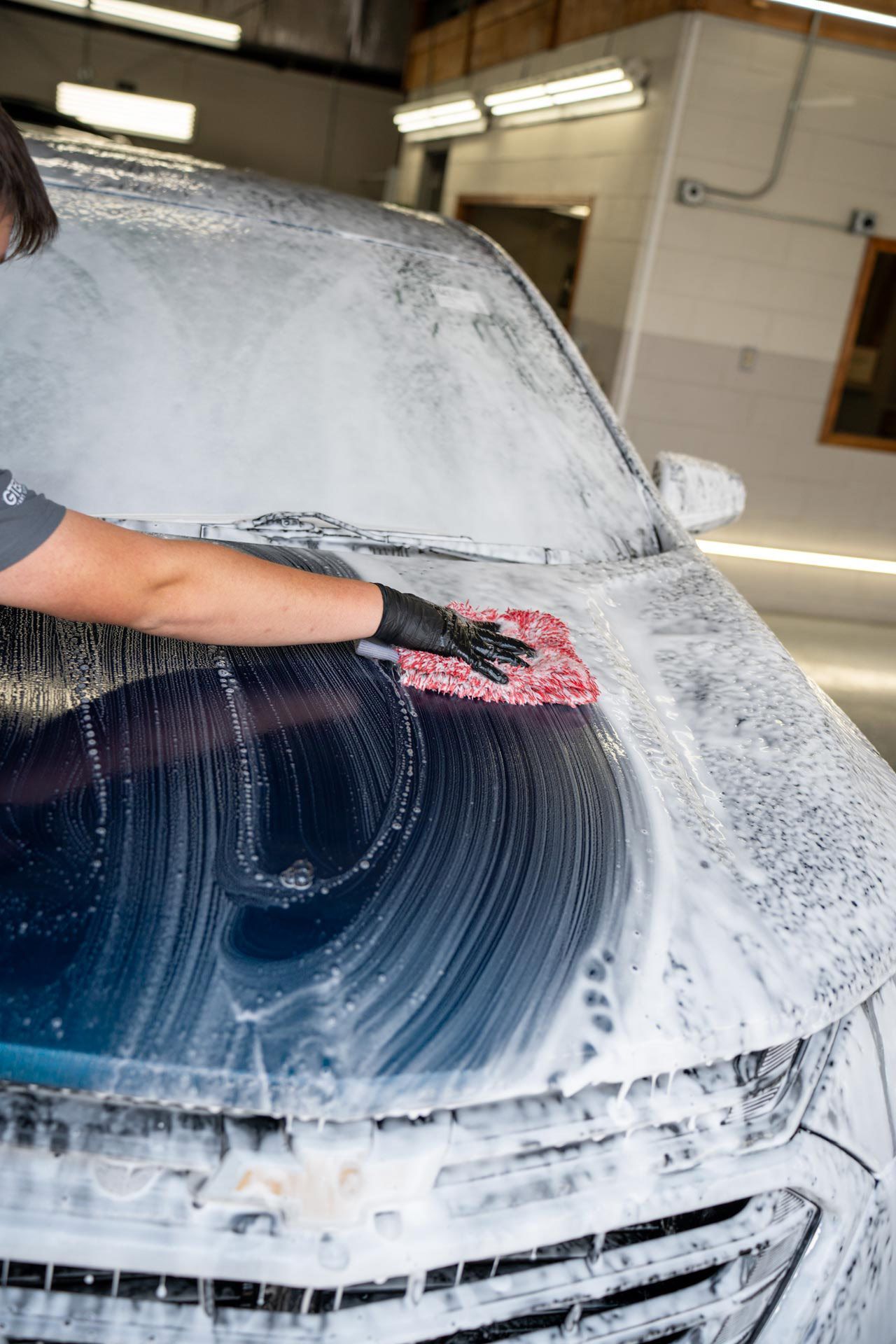 Car covered in soap suds at a car wash, rear view showing taillight and exhaust.