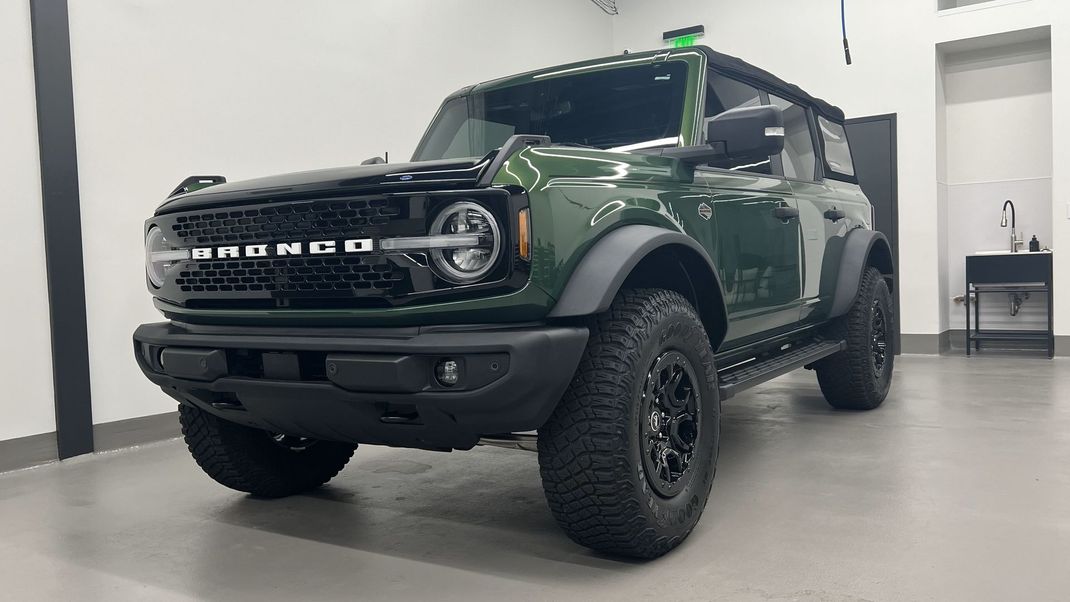 a green ford bronco is parked in a garage .