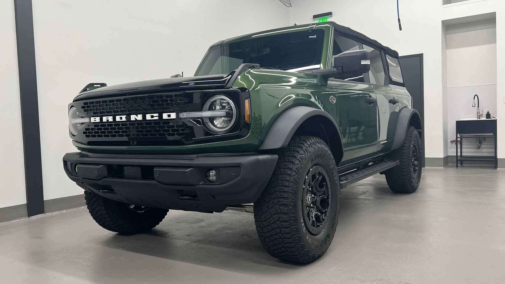 a green ford bronco is parked in a garage .