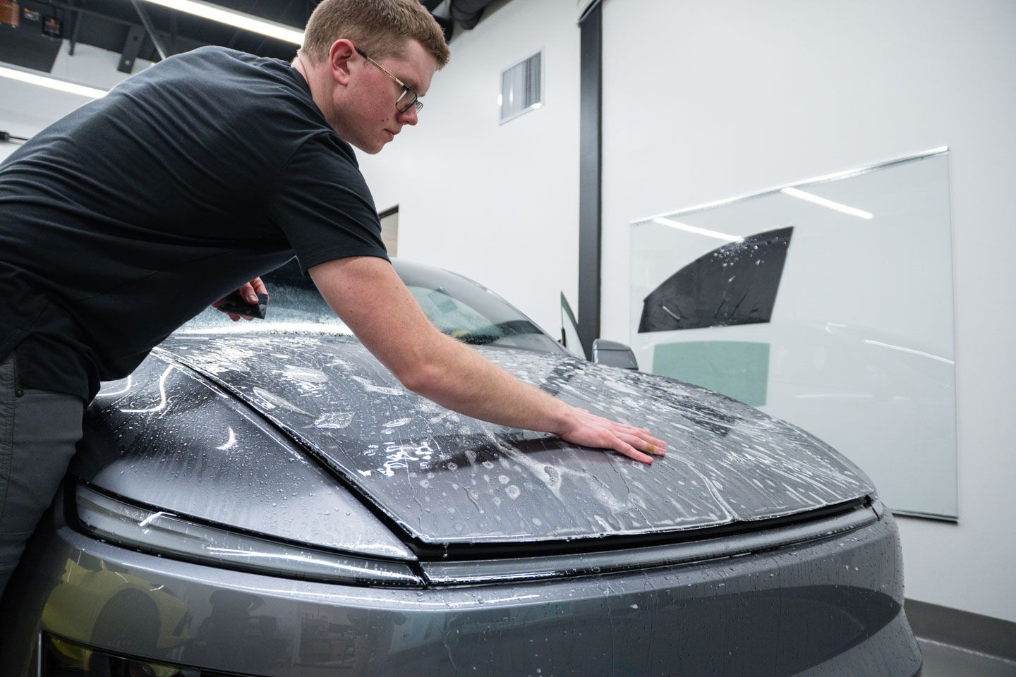 A man is applying a protective film to the hood of a car.