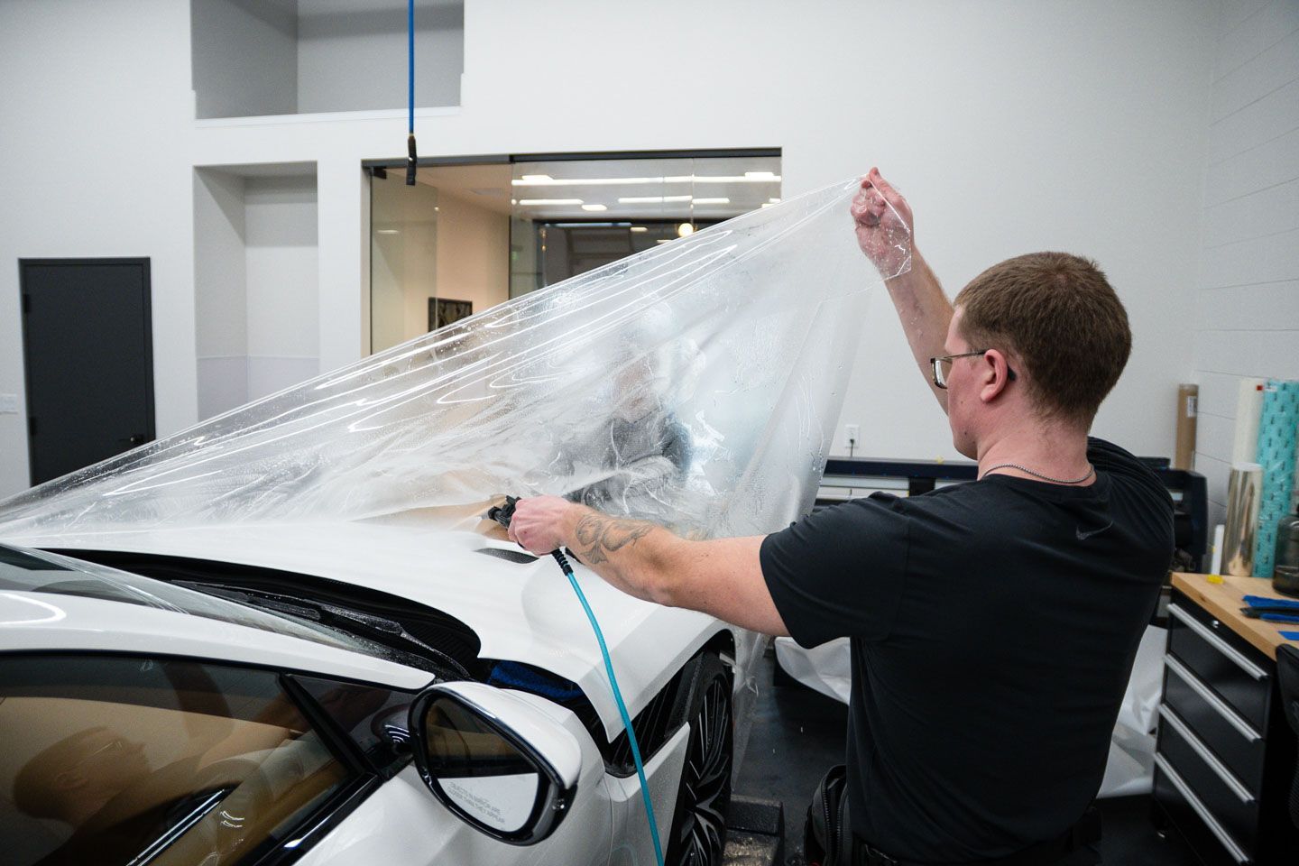 A man is wrapping a car with a plastic sheet.