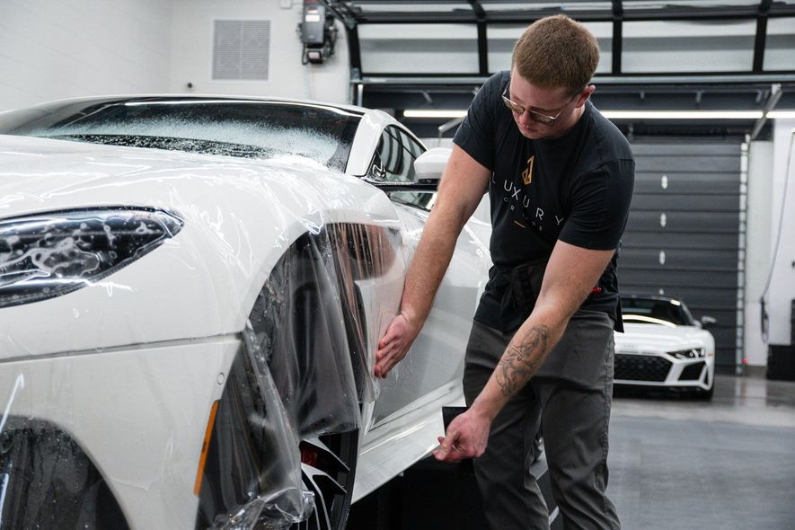 A man is applying a protective film to a white car in a garage.