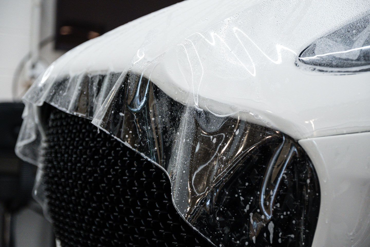 Clear protective film being applied to the front of a white car, covering the grill and bumper.
