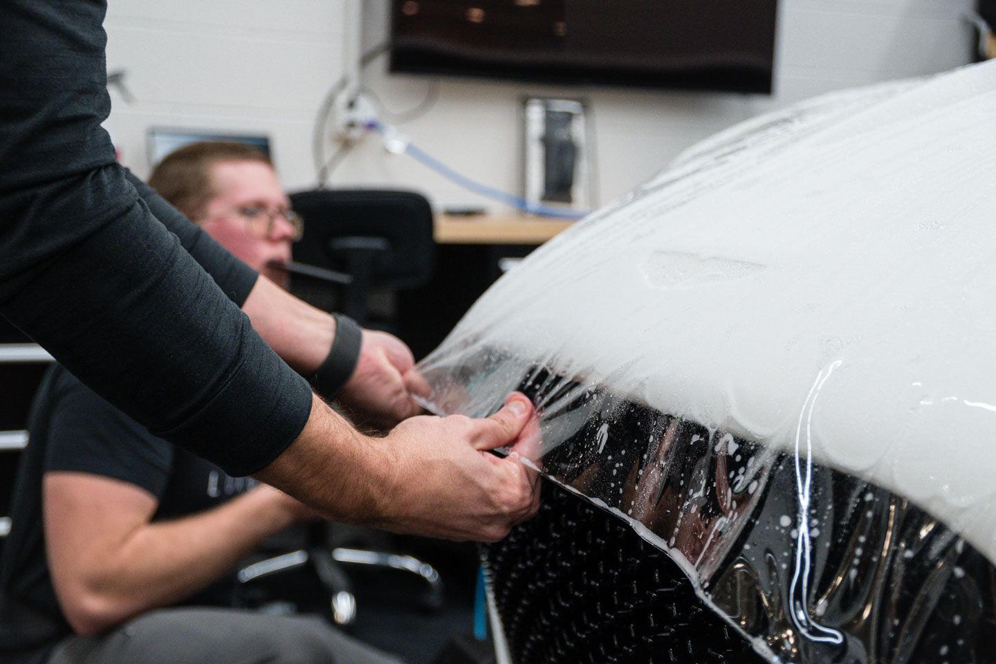 Dark green sports car's hood, with vents, reflected in a showroom window, on a gray floor.